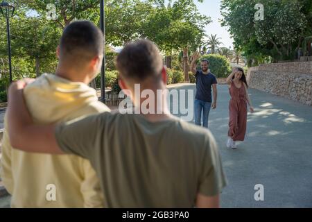 Amici in attesa dei loro amici di arrivare. Stanno arrivando. Indossano colorati abiti estivi. Sono caucasici. Stanno camminando verso Foto Stock