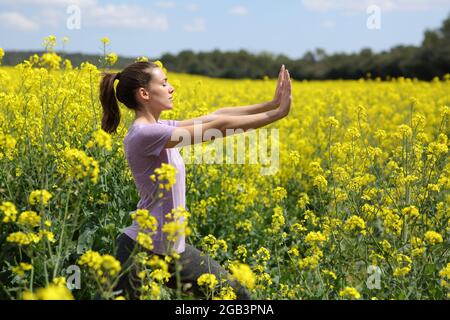 Profilo di una donna che fa esercizio tai chi in piedi in un campo giallo Foto Stock