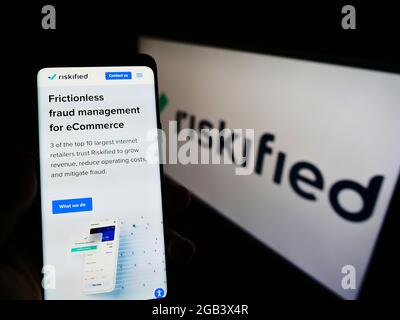 Persona titolare smartphone con sito web della società di software di prevenzione delle frodi Riskified Ltd. Su schermo con logo. Mettere a fuoco il centro del display del telefono. Foto Stock