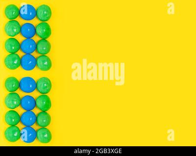 Caramelle colorate su sfondo giallo. Colori della bandiera brasiliana. Disposizione piatta, spazio di copia, vista dall'alto, modello, mockup. Foto Stock