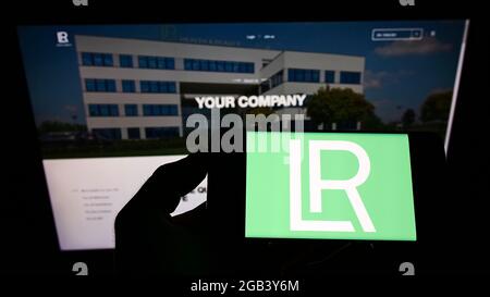 Persona titolare smartphone con logo della società di cosmetici LR Health and Beauty Systems GmbH sullo schermo di fronte al sito web. Mettere a fuoco il display del telefono. Foto Stock