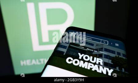 Telefono cellulare con sito web della società di cosmetici LR Health and Beauty Systems GmbH su schermo davanti al logo. Mettere a fuoco in alto a sinistra del display del telefono. Foto Stock