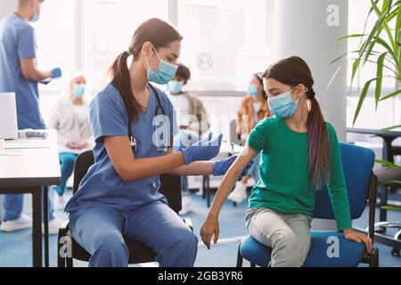 Ragazza che riceve l'iniezione di vaccino Covid seduta con il medico in Clinica Foto Stock