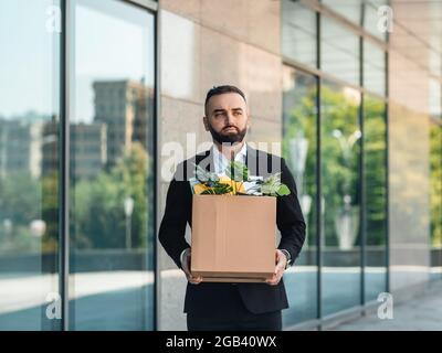 L'uomo è sconvolto dal licenziamento, ha perso il suo lavoro. Infornato lavoratore maschio che si sposta fuori ufficio con scatola piena di effetti personali, spazio di copia Foto Stock