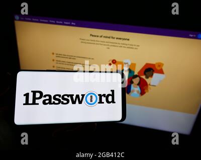 Persona che detiene il cellulare con il logo della società di gestione delle password AgileBits Inc. (1Password) sullo schermo davanti alla pagina web. Mettere a fuoco il display del telefono. Foto Stock