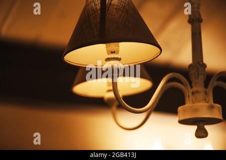 Un bel lampadario elegante con sfumature di tessuto pende nella stanza e brilla di luce calda di notte, creando un'atmosfera accogliente. Un motel. Foto Stock