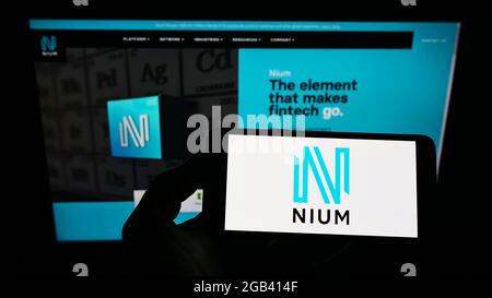 Persona che detiene smartphone con il logo di Singaporean società di pagamento NIUM Pte. Ltd. Sullo schermo di fronte al sito web. Mettere a fuoco il display del telefono. Foto Stock