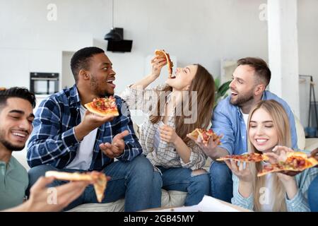 I giovani amici si divertono a mangiare insieme la pizza, a ridere e a chiacchierare a casa Foto Stock