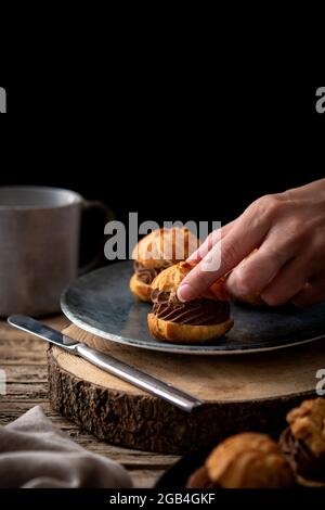 Profiteroles al cioccolato e alla crema su un rustico tavolo in legno Foto Stock