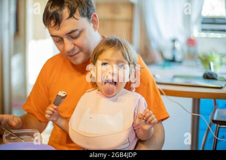 bambino divertente mangiare gelato adorabile bambino mangiare gelato e mostra la lingua. padre che allatta baby lanch Foto Stock