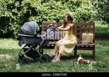 Passeggini per neonati. Giovane madre con neonato in passeggino seduto su panca nel parco. Ritratto esterno di mamma con neonato in Foto Stock