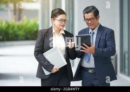 Seri partner aziendali senior che camminano lungo la strada e discutono del contratto sul tablet Foto Stock
