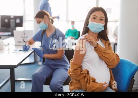 Donna asiatica in gravidanza felice che mostra la mano con Plaster dopo il vaccino Foto Stock