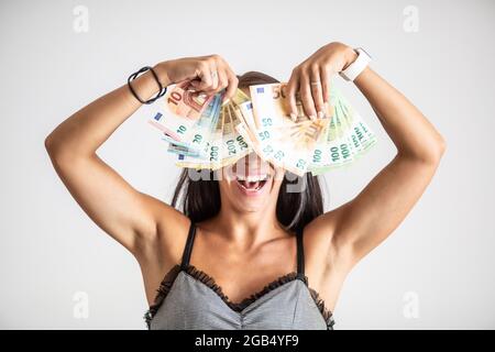 La mano piena di banconote copre il volto di una giovane donna felice. Foto Stock