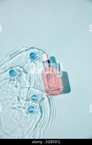 Mockup di bottiglia cosmetica rosa in vetro con pipetta e siero su superficie d'acqua con onde concetto di pubblicità detergente e idratante, invecchiamento nativo s. Foto Stock