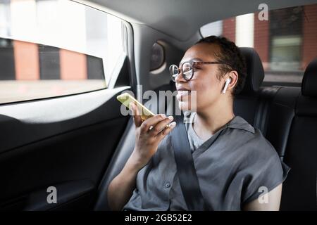 Donna africana felice seduta sul sedile posteriore della macchina che parla sul telefono cellulare e sorridente Foto Stock