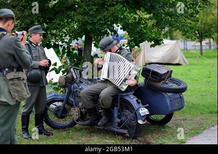 Reenactor vestito in uniforme di soldato tedesco della seconda guerra mondiale seduto su una vecchia motocicletta militare e suonando fisarmonica. 4 ottobre 2012. Kiev, Ukr Foto Stock