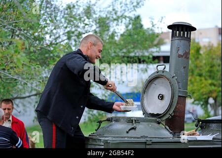 Reenactor vestito in uniforme di marinaio della marina dell'URSS mette il cibo nel piatto dalla cucina mobile del campo. 4 ottobre 2012. Kiev, Ucraina Foto Stock