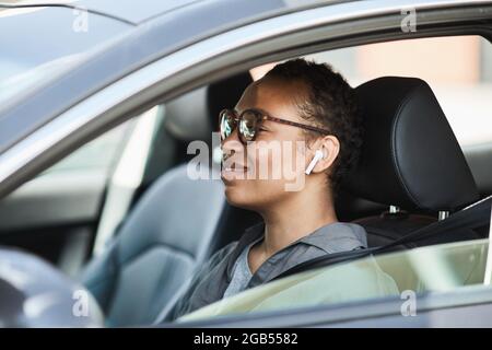 Donna africana felice in cuffie wireless che guida in auto Foto Stock