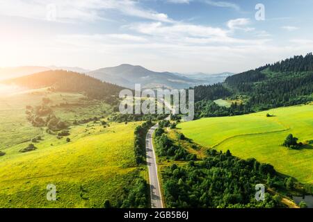 Volo sulle montagne estive con serpente di strada di montagna, campi verdi e foreste. Ucraina, Carpazi. Fotografia di paesaggio Foto Stock
