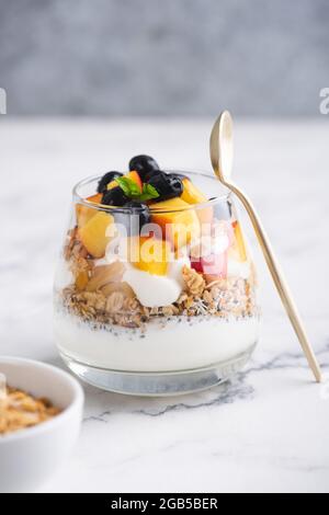Yogurt greco con muesli e frutta in vaso su sfondo bianco di marmo, spazio copia. Cibo sano Foto Stock