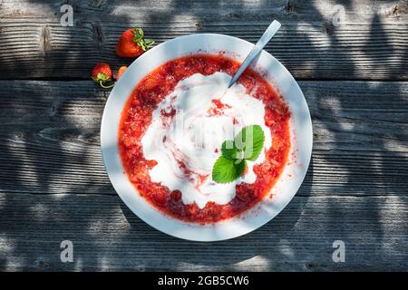 Zuppa di fragole fresche, zucchero e panna acida con foglie di menta su tavola di legno Foto Stock