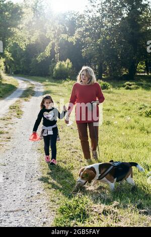 Donna anziana alla moda e la sua bambina godendo una passeggiata in campagna con il loro cane beagle - nonna e nipote felici insieme Foto Stock