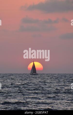 Barca a vela completamente di fronte al sole impostazione al Mar Mediterraneo Foto Stock