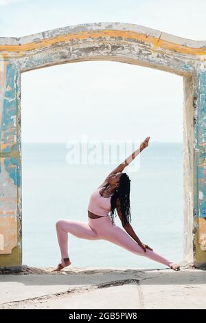 Calzare la giovane donna con la parte superiore rosa e le leggings facendo deep lounge quando si sta sulla roccia sotto l'arco antient Foto Stock