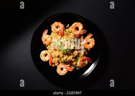 Piatto tradizionale italiano, risotto di pesce, riso con gamberetti, cozze, aglio, vino bianco, prezzemolo su piatto nero. Foto Stock