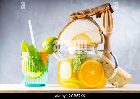 Limonata bevanda di acqua, limone, arancia e foglie di menta in una teiera trasparente. Tè freddo alla menta e pezzi di legno. Composizione creativa Foto Stock