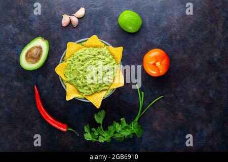 Guacamole con ingredienti e nachos tortilla chips. Guacamole all'avocado con ingredienti pepe, lime e nachos di mais su sfondo scuro. Spazio di copia Foto Stock