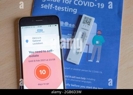 Un iPhone che mostra un messaggio di auto-isolamento durante la pandemia di Covid-19 nel 2021, con un test e un opuscolo Covid negativi. Foto Stock
