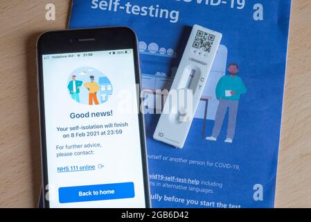 Un iPhone che mostra un messaggio di auto-isolamento durante la pandemia di Covid-19 nel 2021, con un test e un opuscolo Covid negativi. Foto Stock