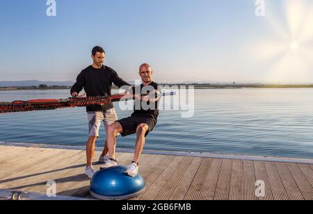 Un windsurfer su una sfera di stabilizzazione stimola la guida su una tavola con espansori di gomma. Sviluppare equilibrio e stabilità. Giorno di sole Foto Stock