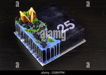 Bella deliziosa torta di compleanno su sfondo di legno scuro, con frutti di bosco e cioccolato fondente. Con numero venticinque. Foto Stock
