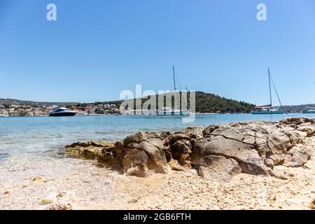 Spiaggia di pietra e sabbia nella popolare destinazione turistica di Rogoznica, piccola città di pescatori nella Dalmazia centrale, Croazia Foto Stock