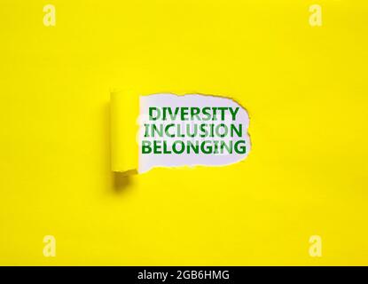 Diversità, inclusione, simbolo di appartenenza. Le parole "diversità, inclusione, appartenenza" appaiono dietro la carta gialla lacerata. Sfondo giallo. Business, subacqueo Foto Stock