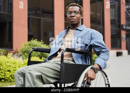 Giovane afroamericano con gambe paralizzate su sedia a rotelle mentre si è in passeggiata Foto Stock