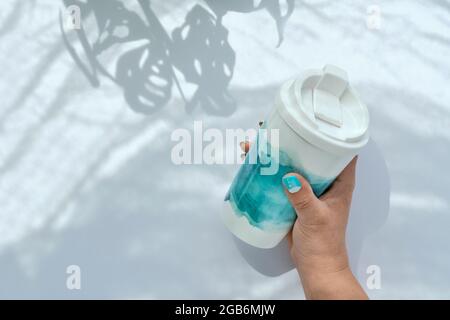 Porta con te una tazza di caffè senza sprechi. I chiodi curati turchesi corrispondono al motivo astratto blu verde sulla tazza. Custodia per le mani, riutilizzabile ed elegante, eco Foto Stock