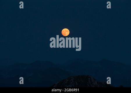 Splendida luna rossa sorge sulle creste montane dell'Appennino. Foto Stock