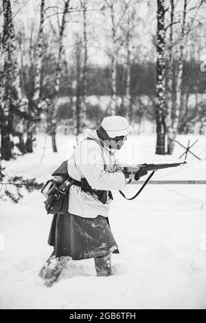 Re-enactor vestito come il soldato tedesco di fanteria Wehrmacht nella seconda guerra mondiale attaccando con fucile nel giorno d'inverno. Rievocazione storica. SECONDA GUERRA MONDIALE. Nero e. Foto Stock