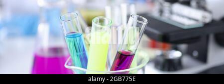 Provette multicolore con liquidi accanto al microscopio Foto Stock
