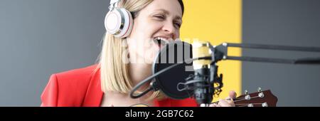 Donna canta e suona la chitarra con le cuffie davanti microfono Foto Stock