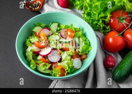 Insalata di verdure fresche in un recipiente di ceramica su sfondo grigio. Piatto estivo di stagione di pomodori, cetrioli e ravanelli. Foto Stock