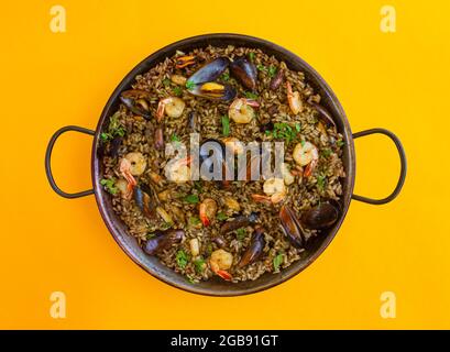 Paella nera con riso, gamberetti, cozze e inchiostro calamari su sfondo giallo Foto Stock