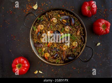 Paella nera con frutti di mare e inchiostro calamaro con pomodori su fondo nero Foto Stock