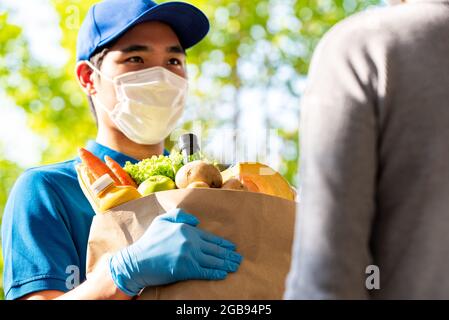 Uomo di consegna asiatico igienico che indossa maschera e guanti mentre consegna generi alimentari al cliente a casa, consegna di cibo in tempo di pandemia concetto Foto Stock