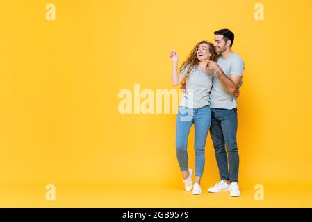 Ritratto a lunghezza intera di giovane coppia interracial felice che si tiene l'un l'altro e che punta le mani per copiare spazio da parte in uno sfondo giallo isolato studio Foto Stock