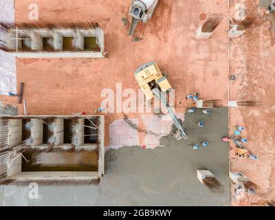 Vista aerea di un grande escavatore con camion in cemento su costruzioni e lavoratori che versano un calcestruzzo bagnato in cantiere, costruzione di calcestruzzo Foto Stock